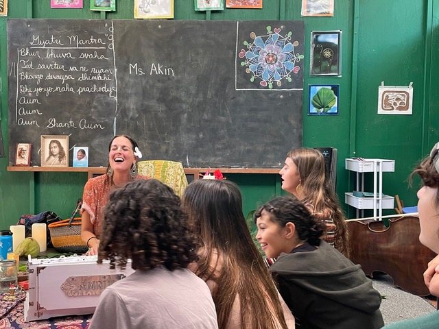 Ashana Sophia teaching children the Gayatri Mantra at a harmonium, laughing